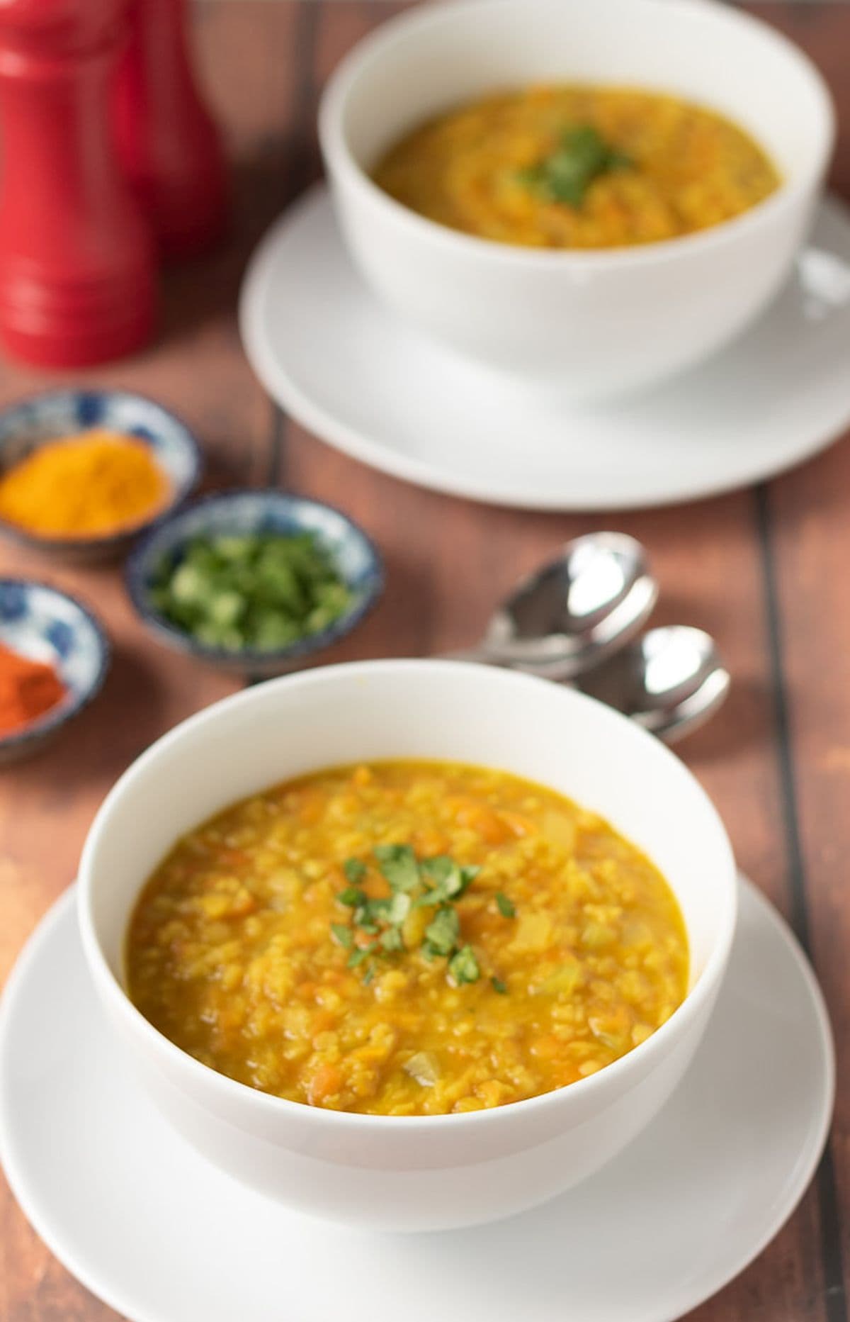 Two delicious bowls of curried red lentil soup with a selection of spices in seperate bowls in between.